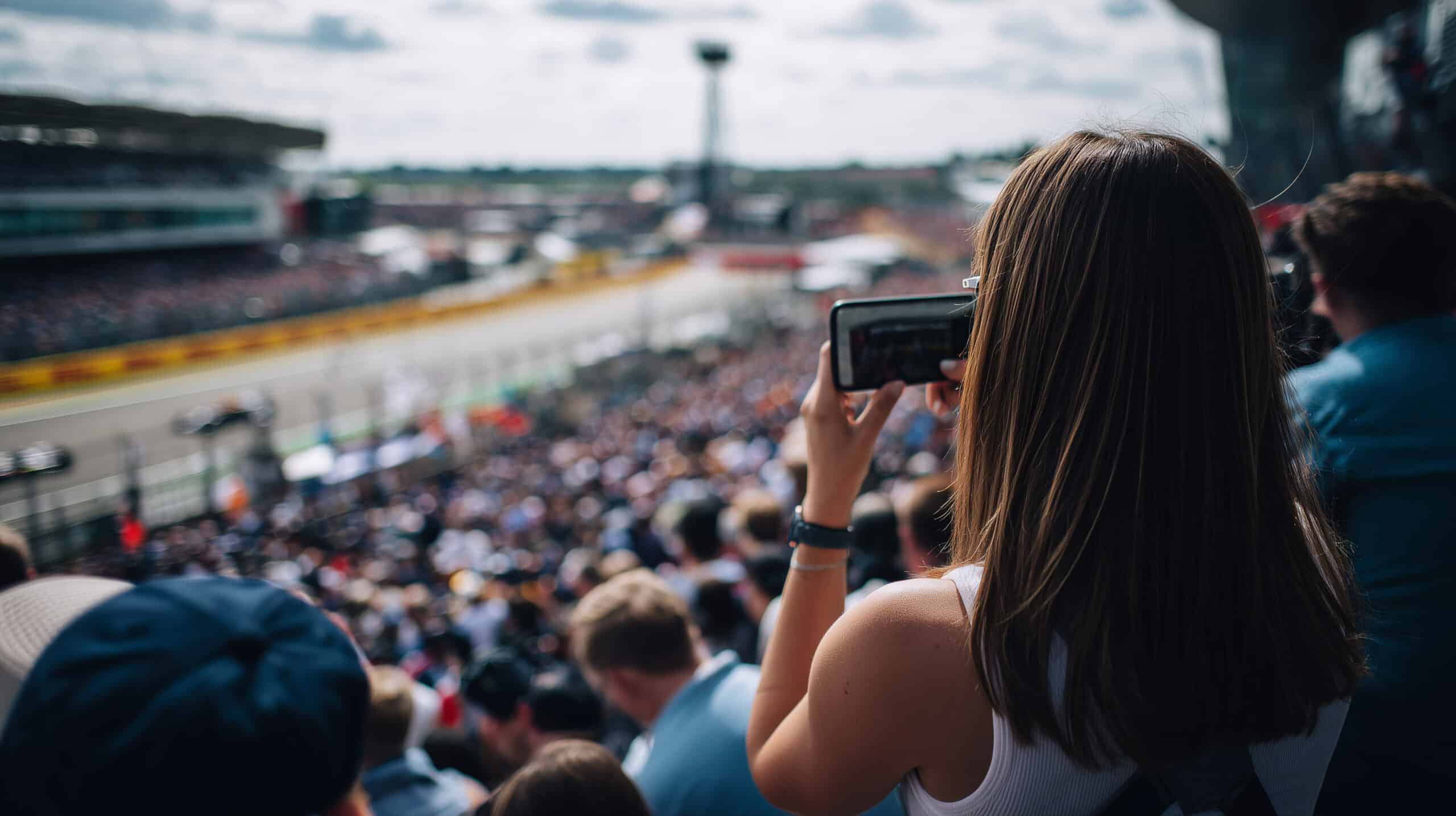 Zuschauer fotografiert den Start eines Autorennens von der Tribüne. Motorsport-Atmosphäre mit Fans bei Formel 1, DTM oder GT3 zum Saisonstart – Spannung, Emotion und Rennfieber pur.